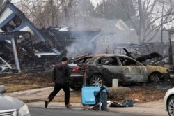 A man walks by the remains of homes, Dec. 31, 2021, after wildfires ripped through a development in Louisville, Colorado.