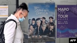 Seorang perempuan berjalan melewati poster yang memperlihatkan anggota grup K-pop BTS di pusat informasi turis di Seoul pada 15 Juni 2022. China menangguhkan pemberian visa bagi warga Korea Selatan yang akan datang ke negara itu.(Foto: AFP/Jung Yeon-je)