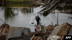 A man carries water bottles as he crosses a destroyed bridge in the frontline town of Bakhmut, in eastern Ukraine's Donetsk region, on Oct. 27, 2022, amid Russia's invasion of Ukraine.