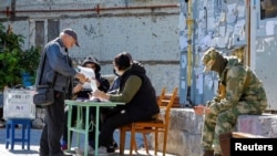 Lokalni stanovnik prima glasački listić od članova izbornog povjerenstva prije nego što ubaci svoj glas u pokretnu glasačku kutiju trećeg dana referenduma o pridruživanju samoproglašene Narodne Republike Donjeck (DNR) Rusiji, u Mariupolju, Ukrajina