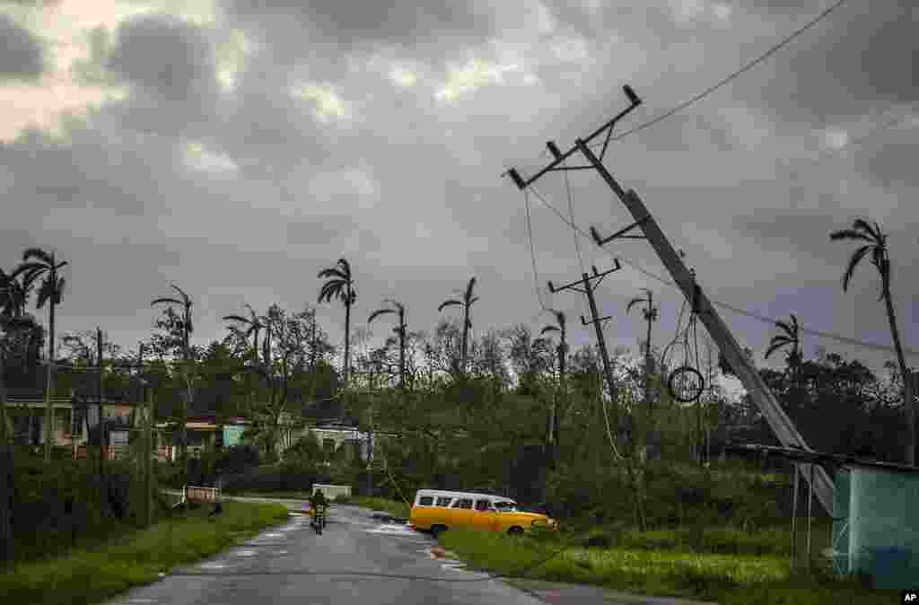 A classic American car drives past utility poles tilted by Hurricane Ian in Pinar del Rio, Cuba, Sept. 27, 2022. 