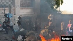 People walk past a burning street barricade during a protest against the government and rising fuel prices in Port-au-Prince, Haiti, Oct. 3, 2022.