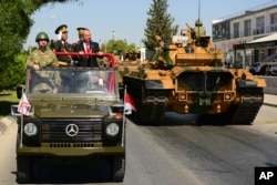 FILE - Turkish Cypriot leader Ersin Tatar, stands on a military vehicle, right, as he reviews the military parade marking the 48th anniversary of the 1974 Turkish invasion in the Turkish occupied area of the divided capital Nicosia, Cyprus, July 20, 2022.