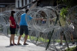 A man shares supplies through barbed wire fence in the coronavirus lockdown area of Selayang Baru, in Kuala Lumpur, Malaysia, on May 3, 2020. Malaysian Prime Minister Muhyiddin Yassin says the economy needs to be revived.