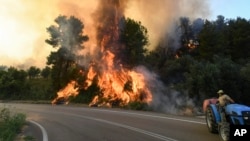 A farmer drives his tractor next to a fire near the village of Krestena, south of Ancient Olympia, about 320 kilometers southwest of Athens, as authorities evacuate villages in the area, July 24, 2022. 