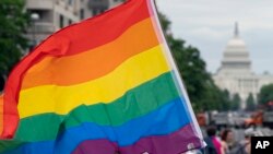 FILE - With the US Capitol in the background, a person waves a rainbow flag as they participant in a rally in support of the LGBTQIA+ community at Freedom Plaza, June 12, 2021, in Washington. 