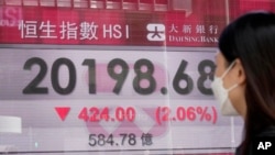 Seorang perempuan mengenakan masker berjalan melewati papan elektronik bank yang menunjukkan indeks saham Hong Kong di Hong Kong, Jumat, 29 Juli 2022. (AP/Kin Cheung)