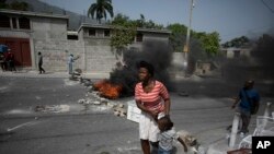 Seorang perempuan beserta anaknya berjalan melewati barikade yang dibuat oleh para demonstran dalam aksi protes kelangkaan BBM di Port-au-Prince, Haiti, pada 13 Juli 2022. (Foto: AP/Odelyn Joseph)