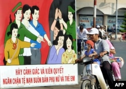 Sebuah keluarga melewati poster yang mengimbau orang-orang untuk waspada dan bertekad menentang perjuangan melawan perdagangan manusia, 24 Februari 2003. (Foto: AFP)