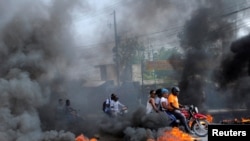 Sejumlah pengendara motor melewati penghalang jalan yang sengaja dibakar dalam konflik antara geng di Port-au-Prince, Haiti, 13 Juli 2022. (Foto: Ralph Tedy Erol/Reuters)