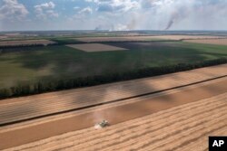 Smoke rises in the background during a fierce battle on the frontline, as a farmer collects harvest in a field in the Dnipropetrovsk region, Ukraine, July 4, 2022.