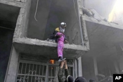 This photo released Feb. 21, 2018, provided by the Syrian Civil Defense group known as the White Helmets, shows a member of the Syrian Civil Defense group rescuing a young girl from a building damaged by airstrikes and shelling by Syrian government forces, in Ghouta, a suburb of Damascus, Syria.