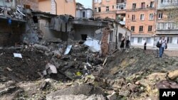 Warga lokal tampak mengamati reruntuhan bangunan yang hancur akibat serangan pasukan Rusia di Kharkiv, pada 11 Agustus 2022. (Foto: AFP/Sergey Bobok)