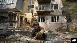 A Ukrainian serviceman collects fragments in the crater to determine the type of ammunition after a Russian attack that damaged some buildings in Kharkiv, Ukraine, Tuesday, Aug. 30, 2022. (AP Photo/Andrii Marienko)