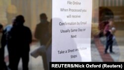 People who lost their jobs are reflected in the door of an Arkansas Workforce Center as they wait in line to file for unemployment following an outbreak of the coronavirus disease (COVID-19), in Fort Smith, Arkansas, U.S. April 6, 2020. (REUTERS/Nick Oxford)