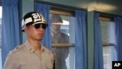 A North Korean soldier looks through a window as a South Korean stands guard during the visit of U.S. Secretary of State Hillary Clinton at the U.N. truce village building that sits on the border of the Demilitarized Zone (DMZ), in Panmunjon, South Korea,