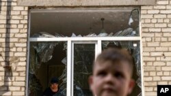 Mfanyakazi akisafisha nyumba wakati Tikhon Pavlov, (11), akipita katika Chuo cha Ufundi na Usanifu wa Majumba, Kramatorsk, alipokuwa anajifunza karate, baada ya shambulizi la roketi asubuhi na mapema huko mji wa Kramatorsk, mkoa wa Donetsk, mashariki ya Ukraine, Aug. 19, 2022.