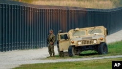 FILE - National Guardsmen stand watch over a fence near the international bridge where thousands of Haitian migrants have created a makeshift camp, in Del Rio, Texas, Sept. 18, 2021.