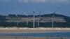 FILE - Beachgoers walk near wind turbines along the coast of Pingtan in Southern China's Fujian province, Aug. 6, 2022. 