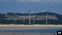 FILE - Beachgoers walk near wind turbines along the coast of Pingtan in Southern China's Fujian province, Aug. 6, 2022. 