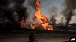 FILE - A man rides his bike past flames and smoke rising from a fire following a Russian attack in Kharkiv, Ukraine, March 25, 2022. 