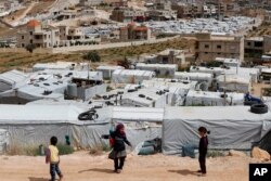 FILE - Syrian refugee children play at an informal refugee camp, which is seen set between the houses and buildings in Arsal, near the border with Syria, east Lebanon, June 13, 2018.