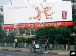 FILE - People walk under a huge advertising billboard of Coca-Cola in downtown Yangon, Myanmar.