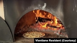 Pizza ທີ່ເປັນສູດຂອງທາງຮ້ານ, ກໍາລັງອົບຢູ່ໃນເຕົາຟືນ ເພື່ອເອົາໄປສົ່ງໃຫ້ລູກຄ້າຕາມການສັ່ງຈອງທາງອອນລາຍ.