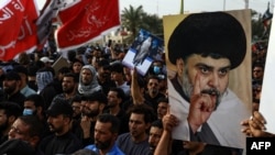 Pendukung ulama Syiah Muqtada al-Sadr membawa potret dirinya saat mereka berkumpul di kota Nasiriyah di Provinsi Dhi Qar selatan Irak, 12 Agustus 2022. (Foto: AFP)