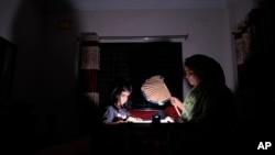 A Bangladeshi woman uses a traditional hand fan as she assists her daughter in her studies during a power cut at their home in Dhaka, Bangladesh, Aug.23, 2022.