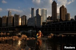 A woman walks in the Jialing river, a tributary of the Yangtze, that is approaching record-low water levels during a regional drought in Chongqing, China, Aug. 20, 2022.