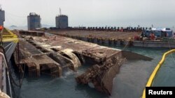 지난 2014년 4월 16일 진도 앞바다에서 침몰한 세월호 선체가 시험 인양에 착수한 지 하룻만인 23일 오전 수면 위로 부상한 모습. 이날 밤 늦게 램프 부분이 바지선과 접촉하는 문제때문에 인양 작업이 일정기간 지연되게 됐다. 