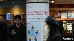 ស្ត្រី​ម្នាក់​ពាក់​ម៉ាស់​ដើរ​នៅ​ជិត​កន្លែង​ដែល​មាន​ដាក់ផ្លាស​សញ្ញា​សាធារណៈ​ដែល​ប្រាប់​ឲ្យ​អ្នក​ដំ​ណើរ​ប្រយ័ត្ន​ចំពោះ​មេរោគ​កូរ៉ូណា នៅ​ព្រលាន​យន្ត​ហោះ​ Heathrow ក្នុង​ទីក្រុង​ឡុងដ៍ ប្រទេស​អង់គ្លេស។