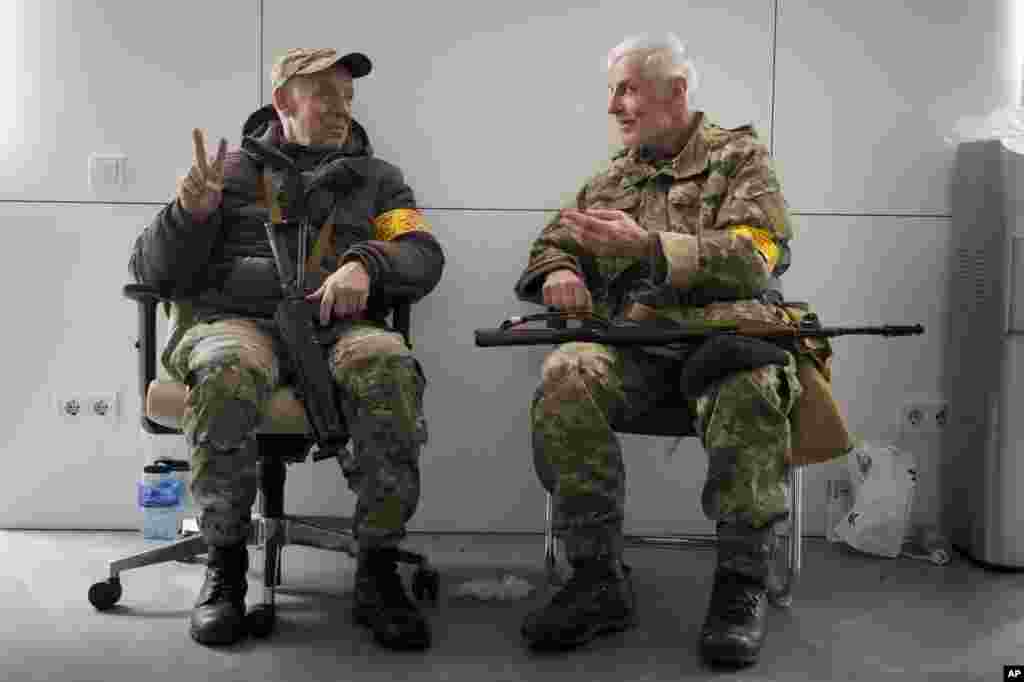 Двајца вооружени лица од цивилната одбрана разговараат меѓу себе во градското собрание во Киев, Украина, недела, 27 февруари 2022 година. Украинските власти соопштија дека руските трупи влегле во вториот по големина град во Украина, Харков. Руските трупи, исто така, извршија зголемен притисок врз стратешките пристаништа на југот на земјата по бранот напади врз аеродромите и постројките за гориво на други места, кои се чинеше дека означуваа нова фаза од руската инвазија. (АП/Ефрем Лукатски)