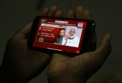 A man in Hyderabad, India watches on his mobile phone Prime Minister Narendra Modi address the nation in a televised speech about COVID-19 situation, April 14, 2020.