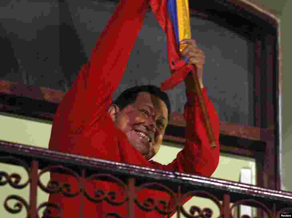 Venezuelan President Hugo Chavez holds the national flag while celebrating from a balcony at the Miraflores Palace in Caracas, October 7, 2012.