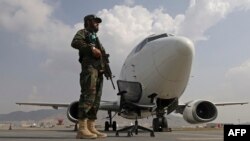 FILE - A Taliban fighter stands guard next to an Ariana Afghan Airlines aircraft on the tarmac at the airport in Kabul, Sept. 12, 2021.