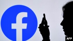 FILE - In this photo illustration, a person looks at a smartphone with a Facebook App logo displayed on the background, in Arlington, Va., Aug. 17, 2021. 