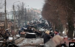 Orang-orang melihat sisa-sisa kendaraan militer Rusia yang hancur di jalan di kota Bucha, dekat Ibu Kota Kyiv, Ukraina, Selasa, 1 Maret 2022. (Foto: AP)