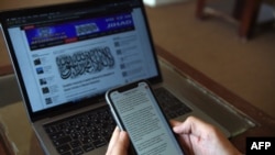 FILE - An Afghan reporter looks at messages sent by a Taliban spokesman, in Kabul, Feb. 6, 2019.