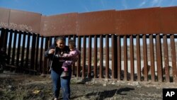 រូបឯកសារ៖ ជនចំណាកស្រុកបីកូននៅជិតជញ្ជាំងព្រំដែនតាមបណ្តោយព្រំដែនអាមេរិក និងម៉ិចស៊ិក។ 