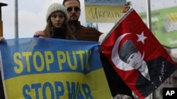 Women with their faces painted in the colors of the Ukrainian flag hold a banner and a Turkish flag with an image of Turkey's founder, Mustafa Kemal Ataturk, as Ukrainians, Turks and Crimean Tatars protest Russia's war in Ukraine, in Ankara, Turkey, March 5