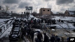 Warga Ukraina melintasi jalan setapak di bawah jembatan yang hancur saat melarikan diri dari Irpin, di pinggiran Kyiv, Ukraina, Selasa, 8 Maret 2022. (AP/Felipe Dana)