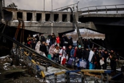 People file across a makeshift river crossing below a destroyed bridge as they flee from advancing Russian troops whose attack on Ukraine continues in the town of Irpin outside Kyiv on March 8, 2022. (Thomas Peter/Reuters)