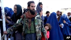 FILE - A Taliban fighter stands guard as people receive food rations distributed by a Saudi humanitarian aid group, in Kabul, Afghanistan, April 25, 2022. 