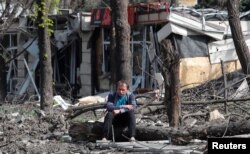 FILE - A man sits in a courtyard near a building damaged during the Ukraine-Russia conflict in the southern port city of Mariupol, Ukraine, April 25, 2022.