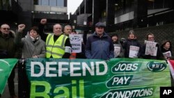 Mick Lynch, Sekjen Serikat Kereta Api, Maritim dan Transportasi (RMT) (jaket biru bertopi), bergabung dengan para pekerja kereta api Inggris selama aksi pemogokan di luar stasiun Euston di London. 