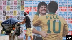 Yon moun pouse yon kabwet ki chaje ak fatra pou resiklaj devan yon miray ki gen foto Foutbole vedet Brezilyen Pele kap bo foutbole vedet Ajanten Diego Maradona nan Sao Paulo, Brezil, Samdi 24 Desanm, 2022. 