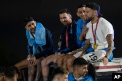 Kapten Lionel Messi (dua dari kiri), duduk bersama Angel de Maria (kedua dari kanan) dan Nicolas Otamendi (kanan), di atas bus yang membawa para pemain dari tim sepak bola Argentina setibanya di bandara Ezeiza, pinggiran kota Buenos Aires, Argentina, Selasa, 20 Desember 2022. (AP Photo/Rodrigo Abd)