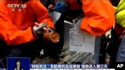 Seorang pekerja darurat memegang perekam "kotak hitam" berwarna oranye yang ditemukan dalam keadaan rusak parah di lokasi kecelakaan penerbangan China Eastern Rabu, 23 Maret 2022, di Kabupaten Tengxian di Daerah Otonomi Guangxi Zhuang, China selatan. (CCTV via AP Video)